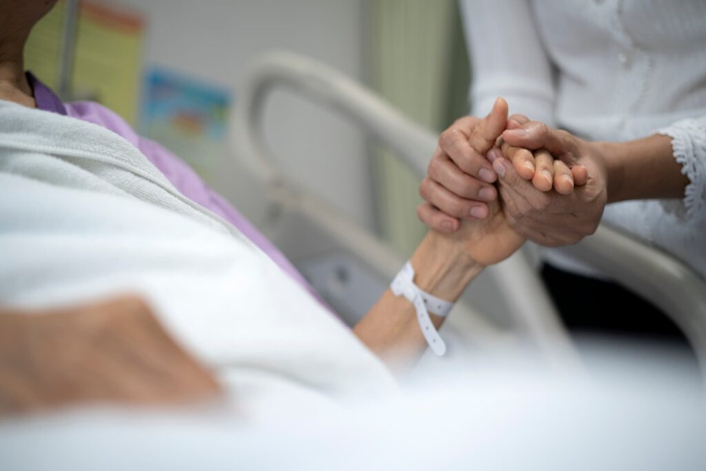 Two people holding hands while one is laying in a hospital bed.