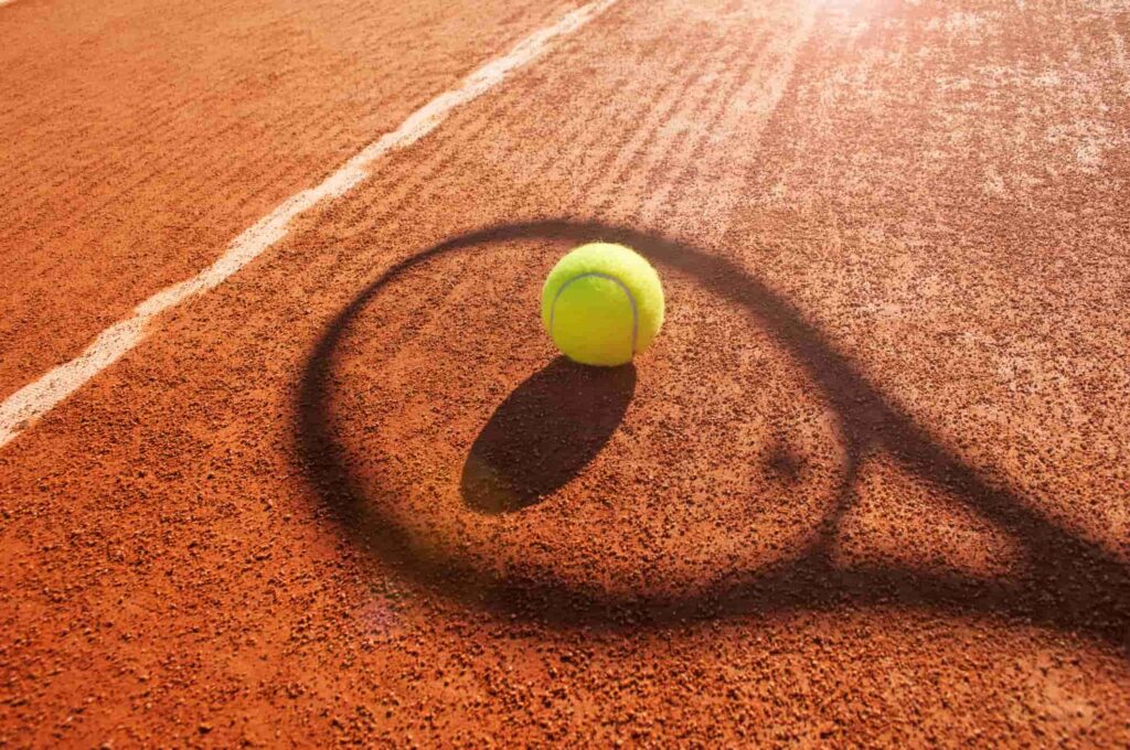 Tennis ball laying on tennis court with a shadow of a tennis raquet.