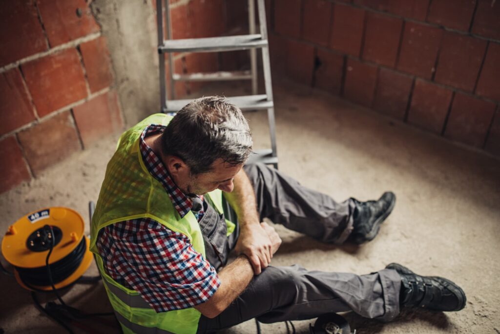 Construction worker sitting on the ground grasping his right wrist. 