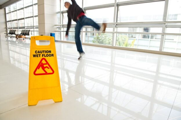 Man slipping on floor. "Caution wet floor" sign placed in front.