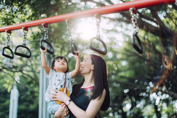 A mother supporting their child on the monkey bar set.