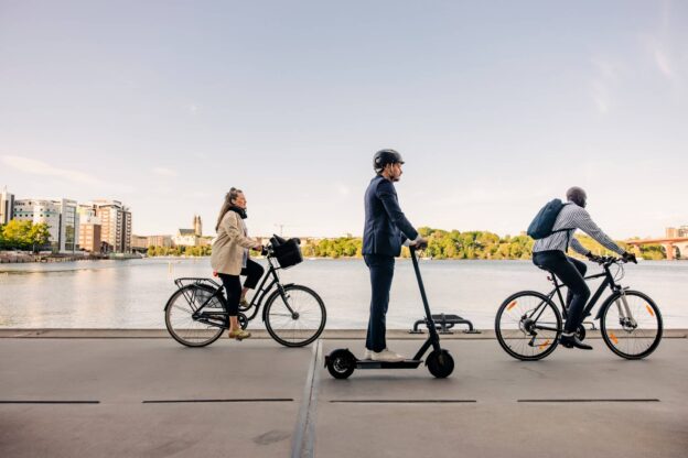 Male and business people commuting through cycles and electric push scooter on promenade