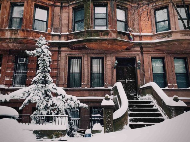 Snow covers a stoop and nearby tree in New York City's Upper West Side townhomes.