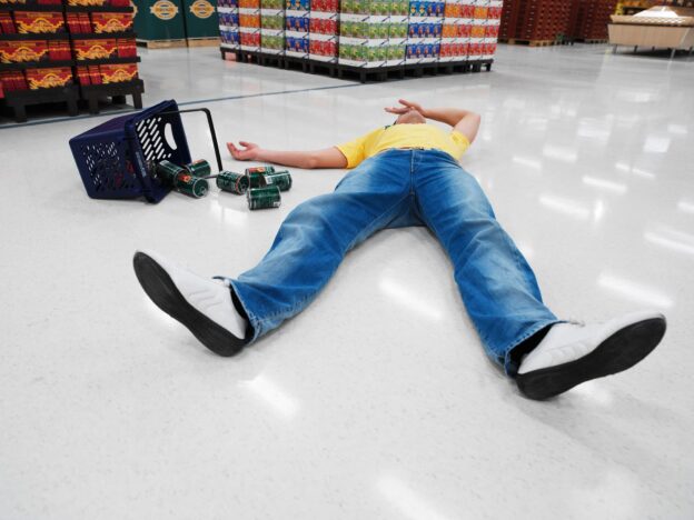 Man slips and falls at a grocery store and is lying on the ground face-up with his hand over his eyes.