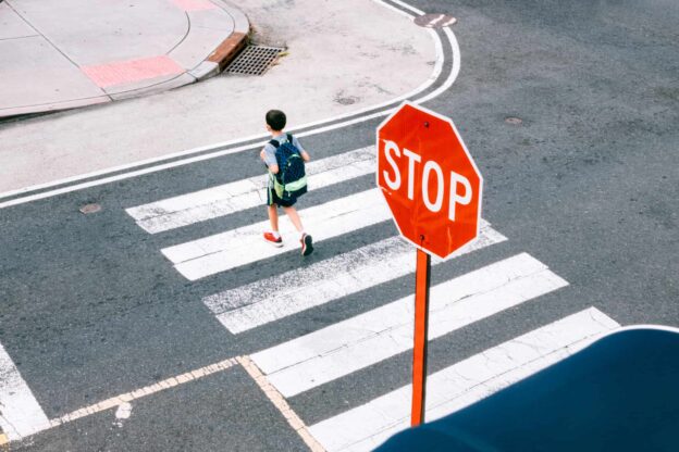 A young pedestrian crossing a city street with a stop sign prominently framed on the right